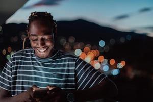 el joven en una calle urbana de la ciudad por la noche enviando mensajes de texto en un teléfono inteligente con bokeh y luces de neón en el fondo. foto
