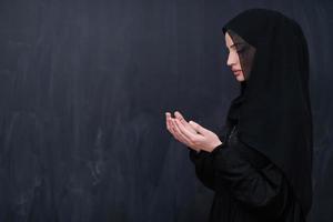 muslim woman making traditional prayer to God in front of black chalkboard photo