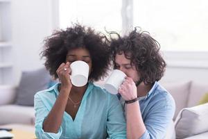 pareja multiétnica sentada en un sofá en casa bebiendo café foto