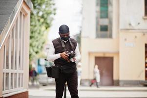 Young professional african american videographer holding professional camera with pro equipment. Afro cameraman wearing black duraq and face protect mask, making a videos. photo