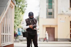 joven camarógrafo afroamericano profesional con cámara profesional con equipo profesional. camarógrafo afro con duraq negro y máscara de protección facial, haciendo videos. foto