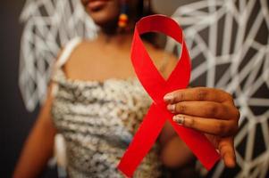 AIDS awareness. Stylish african american woman hold red ribbon against wall with wings. photo