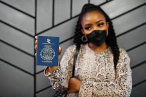 mujer afroamericana con mascarilla negra muestra el pasaporte de Belice en la mano. coronavirus en el país de América, cierre de fronteras y cuarentena, concepto de brote de virus. foto