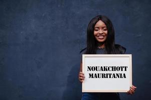 African woman hold white board with Nouakchott Mauritania inscription. Most populous city in Africa concept. photo