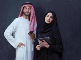 muslim couple using modern technology in front of black chalkboard photo