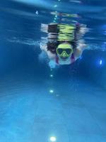 un niño sonriente con gafas nada, se sumerge en la piscina con diversión, salta profundamente bajo el agua. estilo de vida saludable, actividad de deportes acuáticos en los veranos. foto