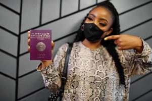 mujer africana con mascarilla negra muestra el pasaporte de etiopía en la mano. coronavirus en el país africano, cierre de fronteras y cuarentena, concepto de brote de virus. foto