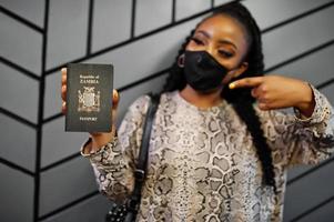 African woman wearing black face mask show Zambia passport in hand. Coronavirus in Africa country, border closure and quarantine, virus outbreak concept. photo