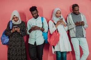A group of African Muslim students use smartphones while standing in front of a pink background photo