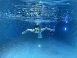 Smiling child in goggles swim, dive in the pool with fun - jump deep down underwater. Healthy lifestyle, people water sport activity on summers. photo