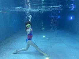 un niño sonriente con gafas nada, se sumerge en la piscina con diversión, salta profundamente bajo el agua. estilo de vida saludable, actividad de deportes acuáticos en los veranos. foto