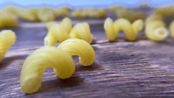 Spiral pasta in brown bowl, scattered pasta on wooden table. Top view video