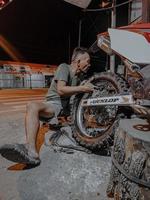 un anciano con pantalones cortos está tratando de cambiar el neumático trasero de la motocicleta por la noche en su taller. foto tomada de noche al aire libre en el pueblo de luhu, gorontalo, el 21 de agosto de 2022