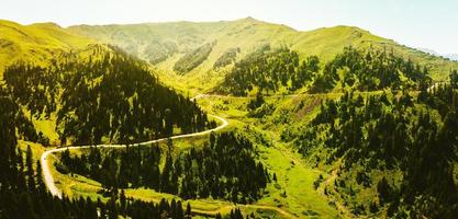 los vehículos con vista aérea conducen viajes en hermosos terrenos montañosos. un coche conduciendo por una carretera asfaltada con un hermoso paisaje de georgia foto