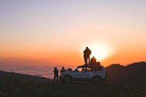 akhmaro, Georgia, 2022 - friends tour group stand on 4wd rooftop watch sunset together outdoors have fun above clouds in famous travel destination photo