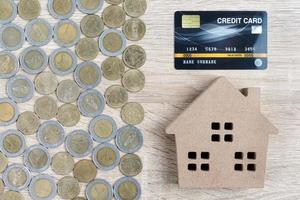 vista superior modelo de casa y monedas con tarjeta de crédito en mesa de madera foto