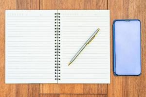Top view image of open notebook with blank pages and cellphone on wooden table photo