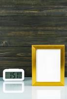 Blank golden frame and digital alarm clock on table photo