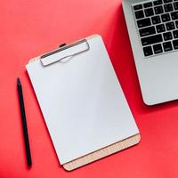 Top view flat lay style of worksapce desk with blank clipboard and laptop on red background with copy space photo