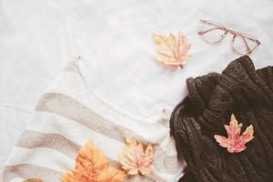 Flat lay of autumn fashion style, sweater, scarf and eyeglasses with maple leaves on white sheet background photo