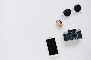 estilo plano creativo con cámara de cine, gafas de sol y teléfono inteligente sobre fondo blanco con espacio de copia foto