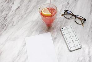 teléfono inteligente y refresco helado con papel en blanco sobre mesa de mármol foto