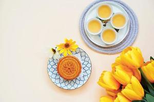 Flat lay of chinese moon cake with hot tea and flower on yellow background, holiday and festival concept