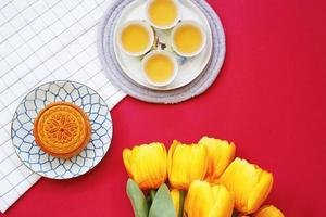 Flat lay of chinese moon cake with hot tea and flower on red background, holiday and festival concept photo