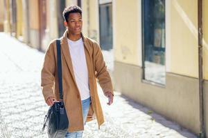 Young black man walking down the street carrying a briefcase and a smartphone. photo