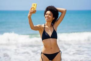 Joyful black woman taking selfie on smartphone near sea photo