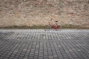 An old red bicycle leans against a brick wall in front of cobblestones, with space for text photo