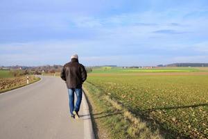 In autumn, a man walks alone on a deserted road that leads over harvested fields, against a blue sky with clouds photo