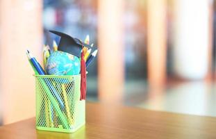 educación aprendizaje y regreso a la escuela con gorra de graduación en una caja de lápices en la mesa en el fondo de la biblioteca - sombrero de graduación en el modelo de globo terráqueo concepto de estudio de educación global foto