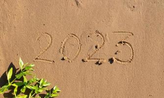 los números 2023 están escritos en la arena de la playa. el concepto del nuevo año. Fondo de feliz año nuevo 2023. viajar durante las vacaciones de navidad. foto