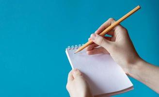 A hand with a pencil writes in a notebook on a blue background. Place for your text photo