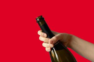 A woman's hand holding an open bottle of champagne on a red background.Holiday concept photo