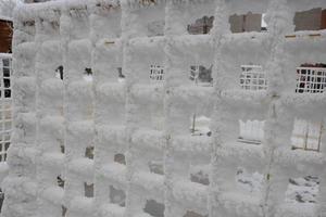 The fence grid is strewn with frost crystals, snowflakes. Winter snowy frosty background. World Snow Day photo