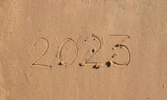los números 2023 están escritos en la arena de la playa. el concepto del nuevo año. Fondo de feliz año nuevo 2023. viajar durante las vacaciones de navidad. foto