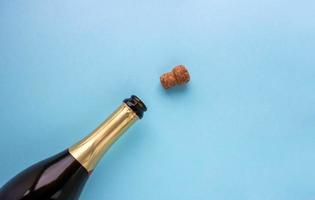 una botella abierta de champán y un corcho sobre un fondo azul. concepto de vacaciones, año nuevo, día de san valentín, 8 de marzo foto