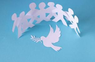 People cut out of paper on a blue background protect the dove of peace.The concept of the World Peace Day photo