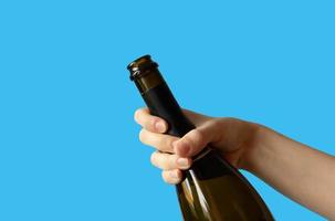 la mano de una mujer sosteniendo una botella abierta de champán sobre un fondo azul.concepto de vacaciones foto