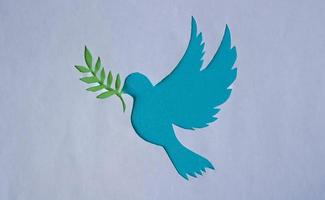 A dove stencil with a twig, cut out of white paper on a blue background for World Peace Day. World Science Day for Peace and Development photo