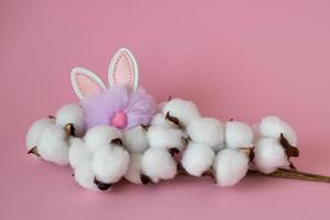 Beautiful white cotton flowers and a small fluffy lilac toy rabbit on a pink background. Easter Concept photo