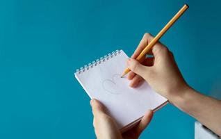 A hand with a pencil writes in a notebook on a blue background. Place for your text photo