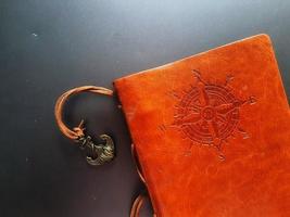 A notebook with a brown leather cover with a compass motif and anchor strap. photo