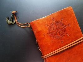 A notebook with a brown leather cover with a compass motif and anchor strap. photo