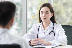 Asian elderly man patient consults with professional woman doctor about his symptom while doctor gives healthcare information with him at hospital. photo