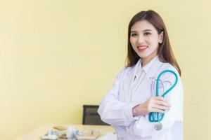 joven y hermosa doctora asiática parada con los brazos cruzados feliz y sonriendo en el hospital. vistiendo una túnica blanca y un estetoscopio foto