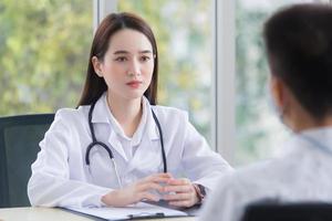 Asian man patient consults with woman doctor about his symptom while doctor gives healthcare information with him at hospital. photo