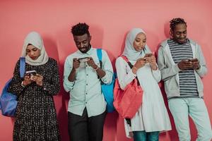 A group of African Muslim students use smartphones while standing in front of a pink background photo